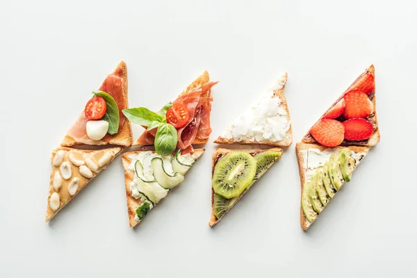 Draufsicht auf Toasts mit Erdbeeren, Avocado, Kiwi und Prosciutto isoliert auf weiß — Stockfoto