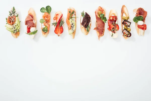 Top view of traditional italian bruschetta with prosciutto, salmon, fruits, vegetables and herbs on white with copy space — Stock Photo