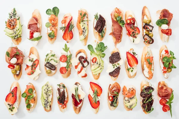 Background of delicious italian bruschetta with salmon, prosciutto, dried tomatoes, avocado, strawberries and herbs on white — Stock Photo