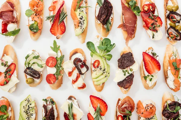 Fondo de deliciosa bruschetta italiana con salmón, jamón, tomates secos, aguacate, fresas y hierbas sobre blanco - foto de stock