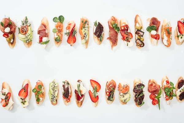 Vista dall'alto di deliziose bruschette tradizionali italiane con prosciutto, salmone, frutta, verdura ed erbe su bianco — Foto stock