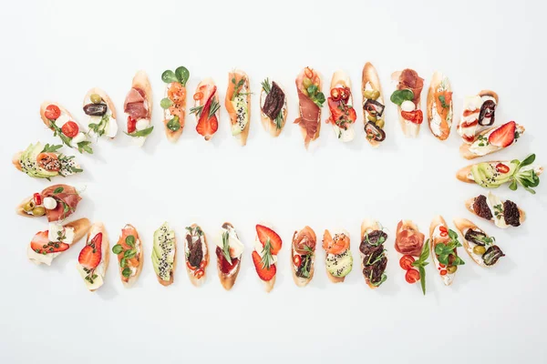 Top view of arranged italian bruschetta with prosciutto, salmon, fruits, vegetables and herbs on white — Stock Photo