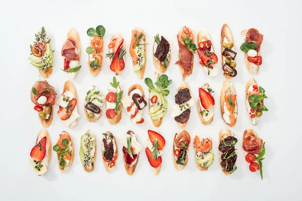 Background of traditional italian bruschetta with salmon, prosciutto, dried tomatoes, avocado, strawberries and herbs on white — Stock Photo