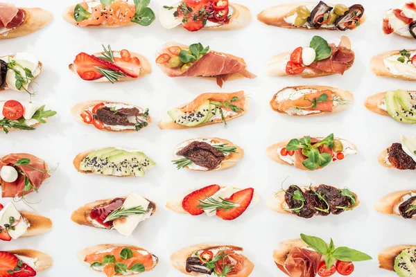 Background of traditional italian bruschetta with salmon, prosciutto, dried tomatoes, avocado, strawberries and herbs on white — Stock Photo