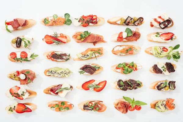 Background of italian bruschetta with salmon, prosciutto, dried tomatoes, avocado, strawberries and herbs on white — Stock Photo