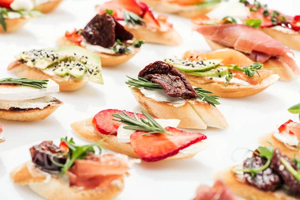 Enfoque selectivo de bruschetta italiana con tomates secos, prosciutto, aguacate, fresas y hierbas - foto de stock