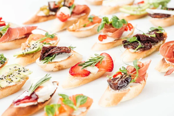 Focus selettivo della bruschetta italiana con pomodori secchi, prosciutto, avocado, fragole ed erbe aromatiche — Foto stock