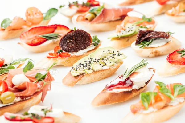 Enfoque selectivo de bruschetta italiana con tomates secos, aguacate, jamón y hierbas - foto de stock