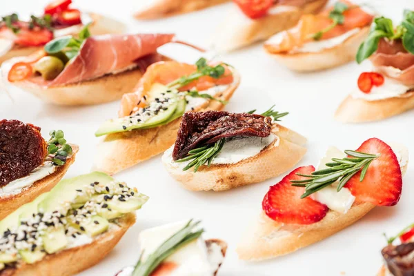 Enfoque selectivo de bruschetta italiana con tomates secos, prosciutto, aguacate, fresas y hierbas en blanco - foto de stock