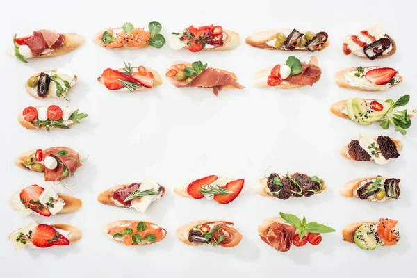 Vue du haut du cadre en bruschetta italienne traditionnelle avec prosciutto, saumon, fruits, légumes et herbes sur blanc — Photo de stock