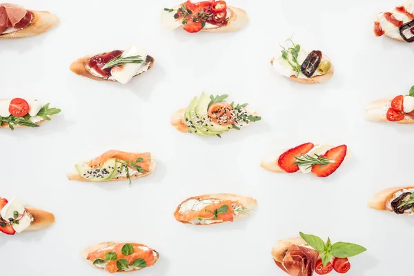 Background of italian bruschetta with salmon, prosciutto, avocado, strawberries and herbs on white — Stock Photo