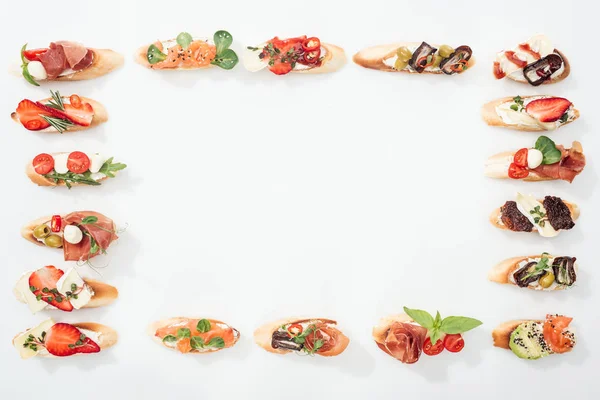 Top view of frame made of traditional italian bruschetta with prosciutto, salmon, fruits, vegetables and herbs on white with copy space — Stock Photo