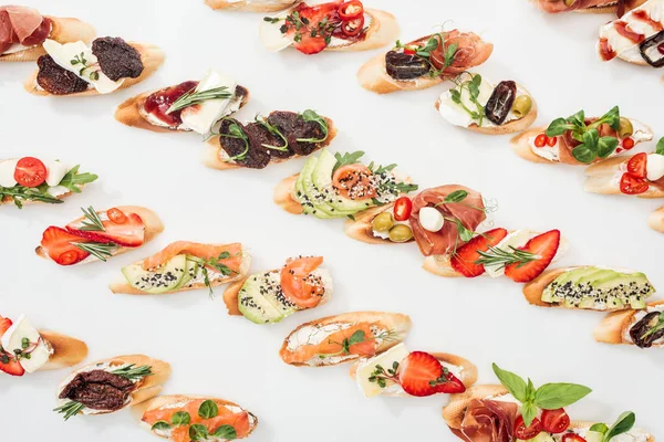 Hintergrund italienischer Bruschetta mit Lachs, Prosciutto, getrockneten Tomaten, Avocado, Erdbeeren und Kräutern auf weißem Hintergrund — Stockfoto