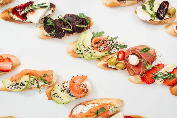 Draufsicht auf traditionelle italienische Bruschetta mit Avocado, getrockneten Tomaten, Prosciutto, Lachs und Kräutern auf Weiß — Stockfoto