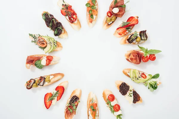 Vista superior de marco redondo hecho de bruschetta italiana tradicional con salmón, jamón, hierbas y varias frutas con verduras - foto de stock