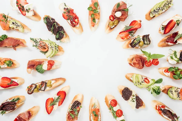 Top view of round frame made of italian bruschetta with salmon, prosciutto, herbs and various fruits with vegetables on white — Stock Photo