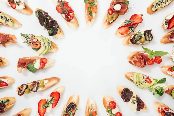 Вид сверху на круглую рамку из итальянской брускетты с лососем, ветчиной, травами и различными фруктами с овощами на белом — стоковое фото