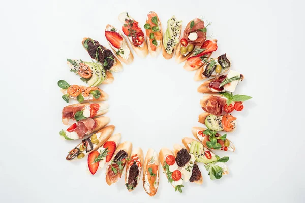 Top view of round frame made of delicious italian bruschetta with salmon, prosciutto, herbs and various fruits with vegetables — Stock Photo