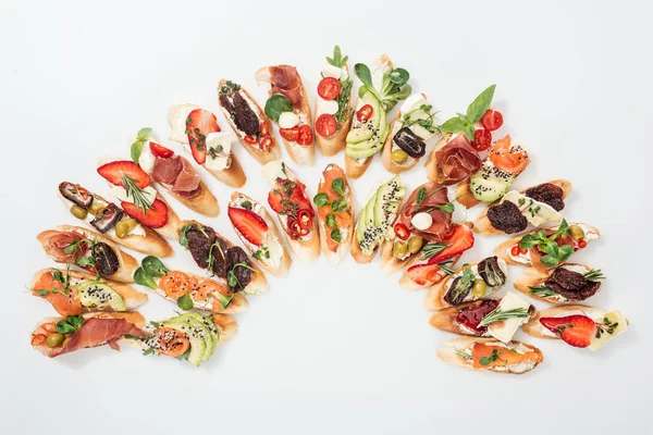 Vista superior de la tradicional bruschetta italiana con jamón, salmón, frutas, verduras y hierbas sobre blanco - foto de stock