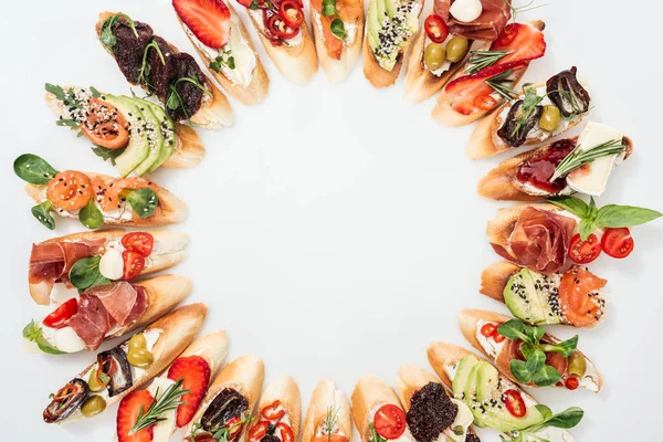 Vue de dessus du cadre rond en délicieuse bruschetta italienne avec saumon, prosciutto, herbes et divers fruits aux légumes — Photo de stock