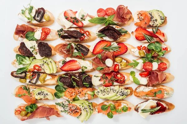 Background of tasty italian bruschetta with salmon, prosciutto, dried tomatoes, avocado, strawberries and herbs on white — Stock Photo