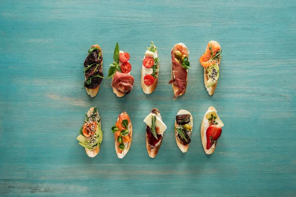 Top view of italian bruschetta with salmon, dried tomatoes, prosciutto and herbs on wooden table — Stock Photo