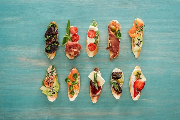 Top view of italian bruschetta with salmon, dried tomatoes, prosciutto and herbs on wooden table — Stock Photo