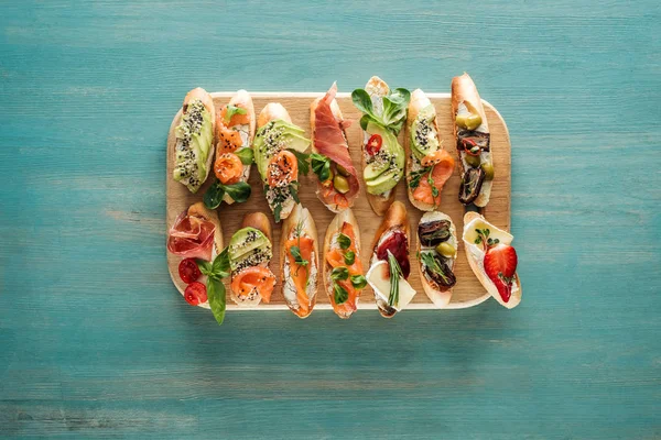 Top view of italian bruschetta with prosciutto, salmon and vegetables on chopping board — Stock Photo