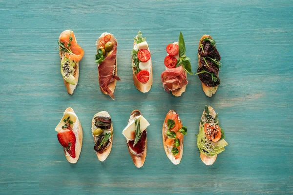 Top view of italian bruschetta with salmon, dried tomatoes, prosciutto and herbs on wooden table — Stock Photo