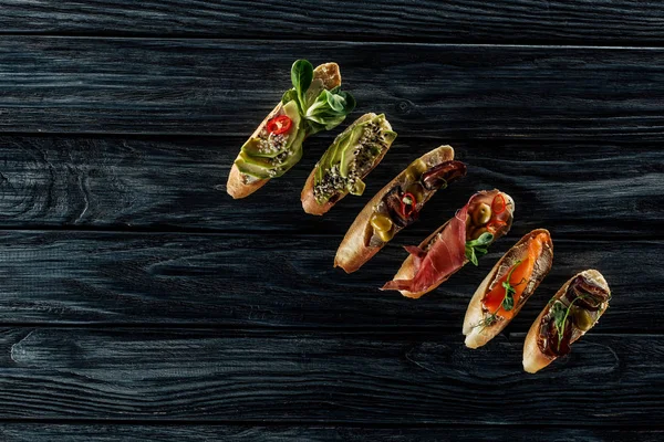 Vista superior de la bruschetta italiana con salmón, jamón y aguacate sobre mesa de madera - foto de stock