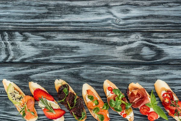 Top view of italian bruschetta with strawberries, salmon, herbs and prosciutto on wooden table — Stock Photo