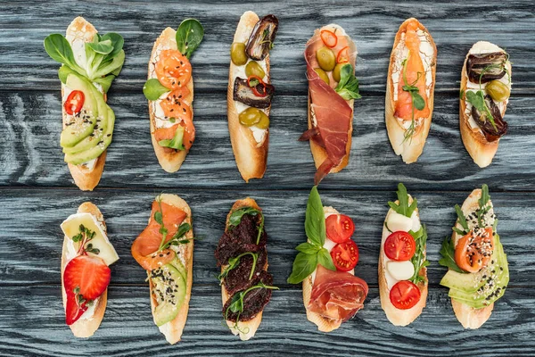 Vue de dessus de bruschetta italienne avec prosciutto, saumon et légumes sur la surface en bois — Photo de stock
