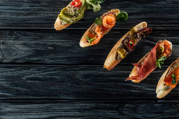 Top view of italian bruschetta with salmon, prosciutto and olives on wooden table — Stock Photo