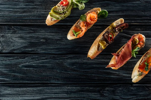 Vista superior de la bruschetta italiana con salmón, jamón y aceitunas sobre mesa de madera - foto de stock