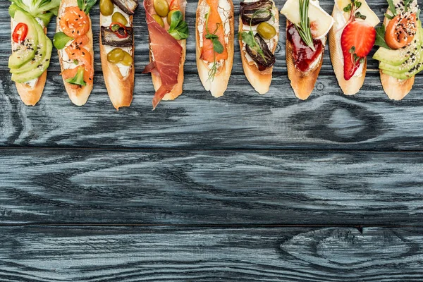 Top view of italian bruschetta with prosciutto, herbs, salmon and vegetables on wooden table with copy space — Stock Photo