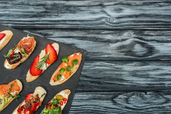 Vue du dessus de la bruschetta italienne aux fraises, au saumon et au prosciutto sur planche à découper avec espace pour copier — Photo de stock