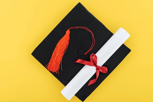 Vue du dessus du chapeau académique et du diplôme avec ruban rouge isolé sur jaune — Photo de stock