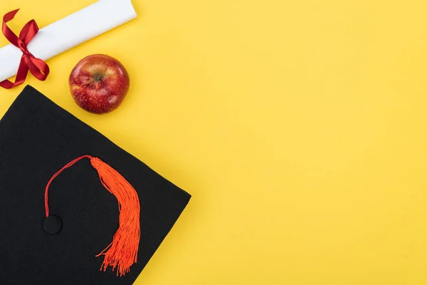 Top view of academic cap, diploma and red apple on yellow surface — Stock Photo