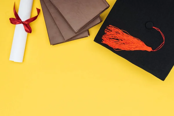 Ansicht von Büchern, akademischer Mütze und Diplom auf gelber Oberfläche — Stockfoto