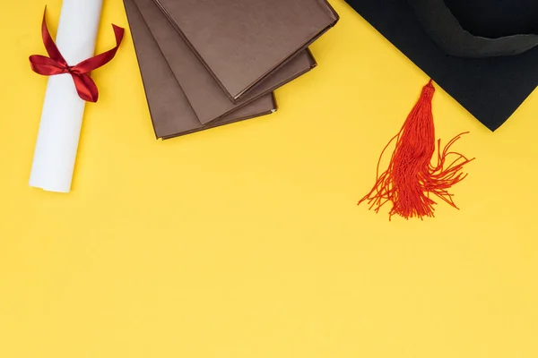 Vista superior de libros, gorra académica y diploma en superficie amarilla - foto de stock