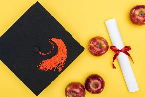 Vue du dessus du chapeau académique, du diplôme et des pommes sur la surface jaune — Photo de stock