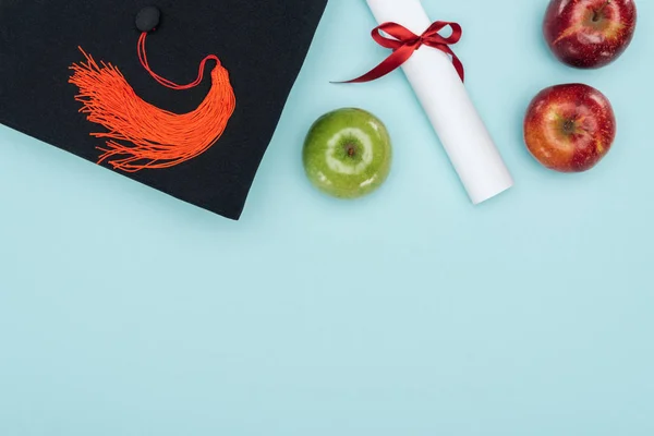 Draufsicht auf akademische Mütze, Diplom und Äpfel auf blauer Oberfläche — Stockfoto