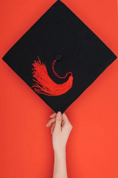 Cropped view of woman holding academic cap on red — Stock Photo