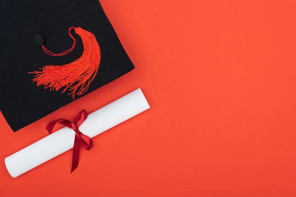 Vista superior de gorro acadêmico e diploma isolado em vermelho — Fotografia de Stock