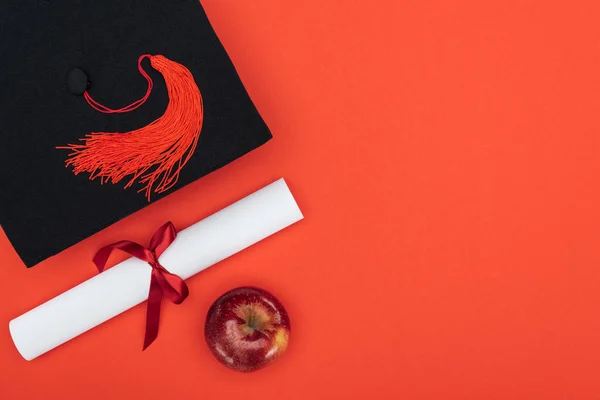 Top view of academic cap, diploma and apple on red surface — Stock Photo