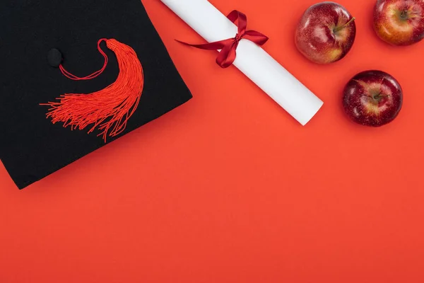 Top view of academic cap, diploma and apples on red surface — Stock Photo