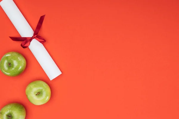 Top view of diploma and green apples on red surface — Stock Photo