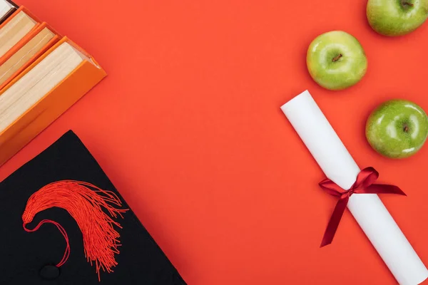 Vista superior de la tapa académica, libros, diploma y manzana en la superficie roja - foto de stock