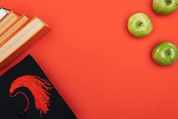 Top view of academic cap, books and apple on red surface — Stock Photo