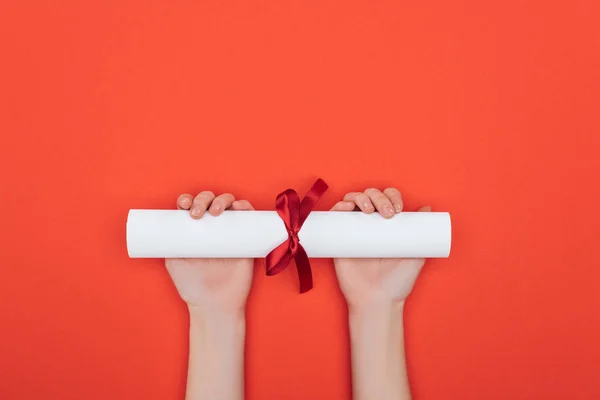 Vista recortada de la mujer que sostiene el diploma con cinta en la superficie roja - foto de stock